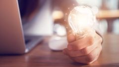 Close-up of a light bulb, held by a woman who uses a laptop.